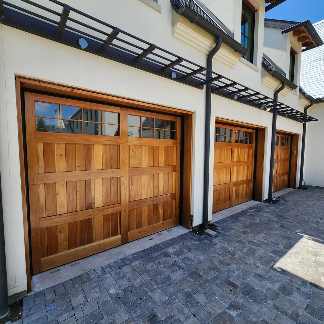 Three stained cedar garage doors on a white stucco home